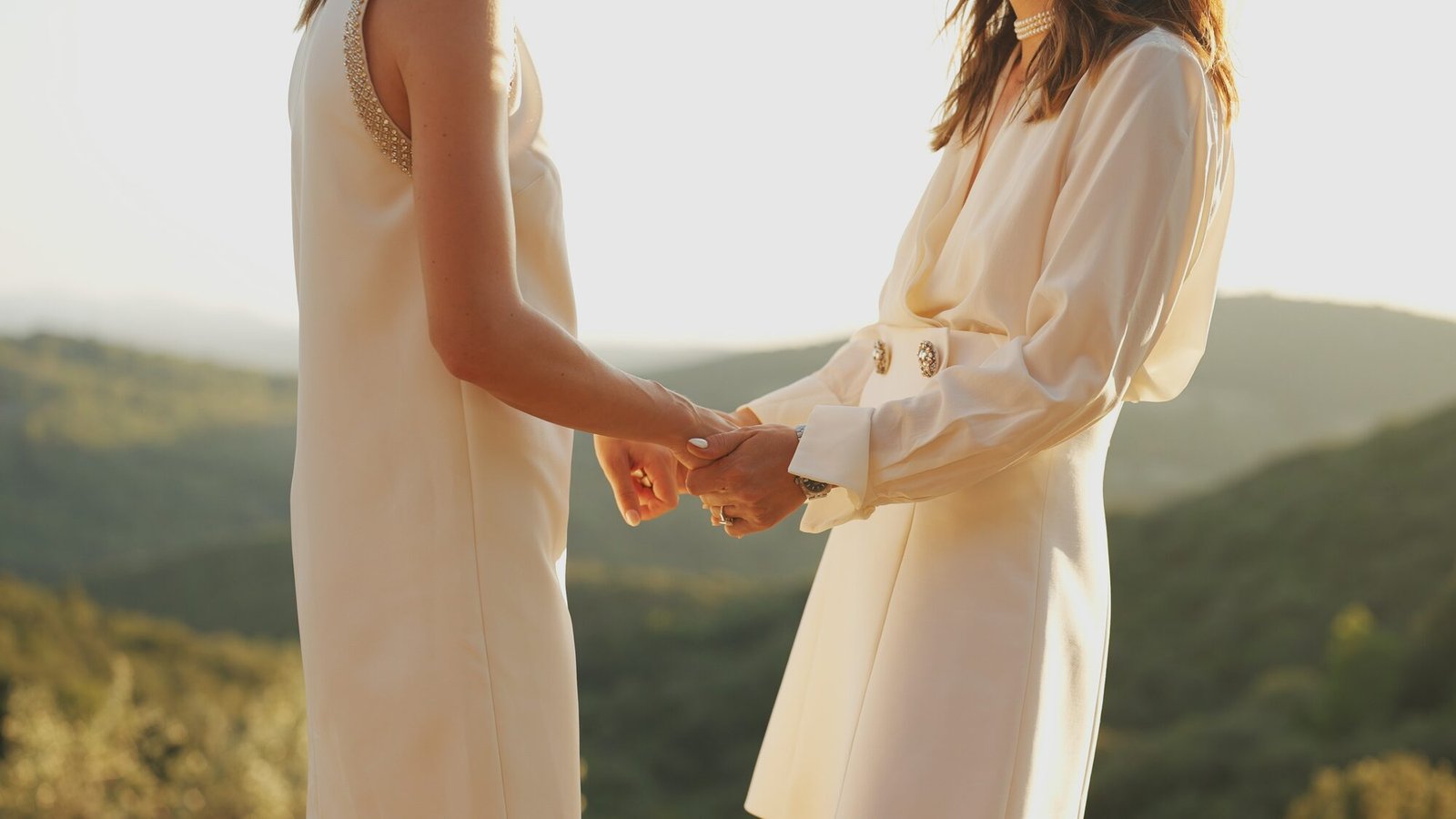Two brides holding hands against the Tuscan hills at sunset before their wedding ceremony at Castello di Vicarello