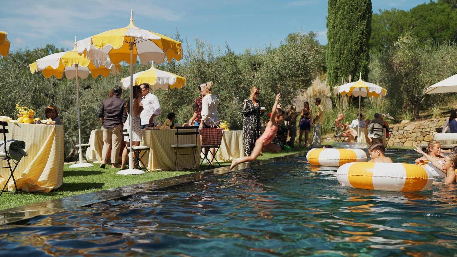 Wedding guests swimming and relaxing by the pool under yellow umbrellas among the olive trees of Castello di Vicarello