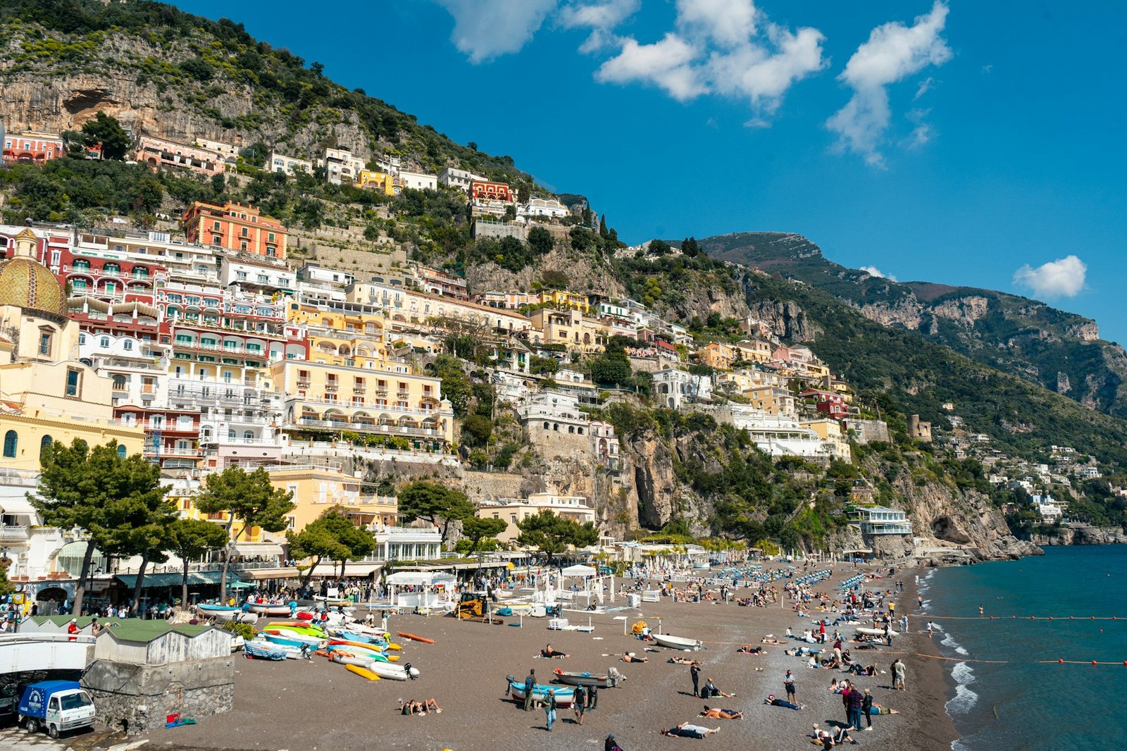 Positano beach town on the Amalfi Coast with blue water and green hillsides in warm season light
